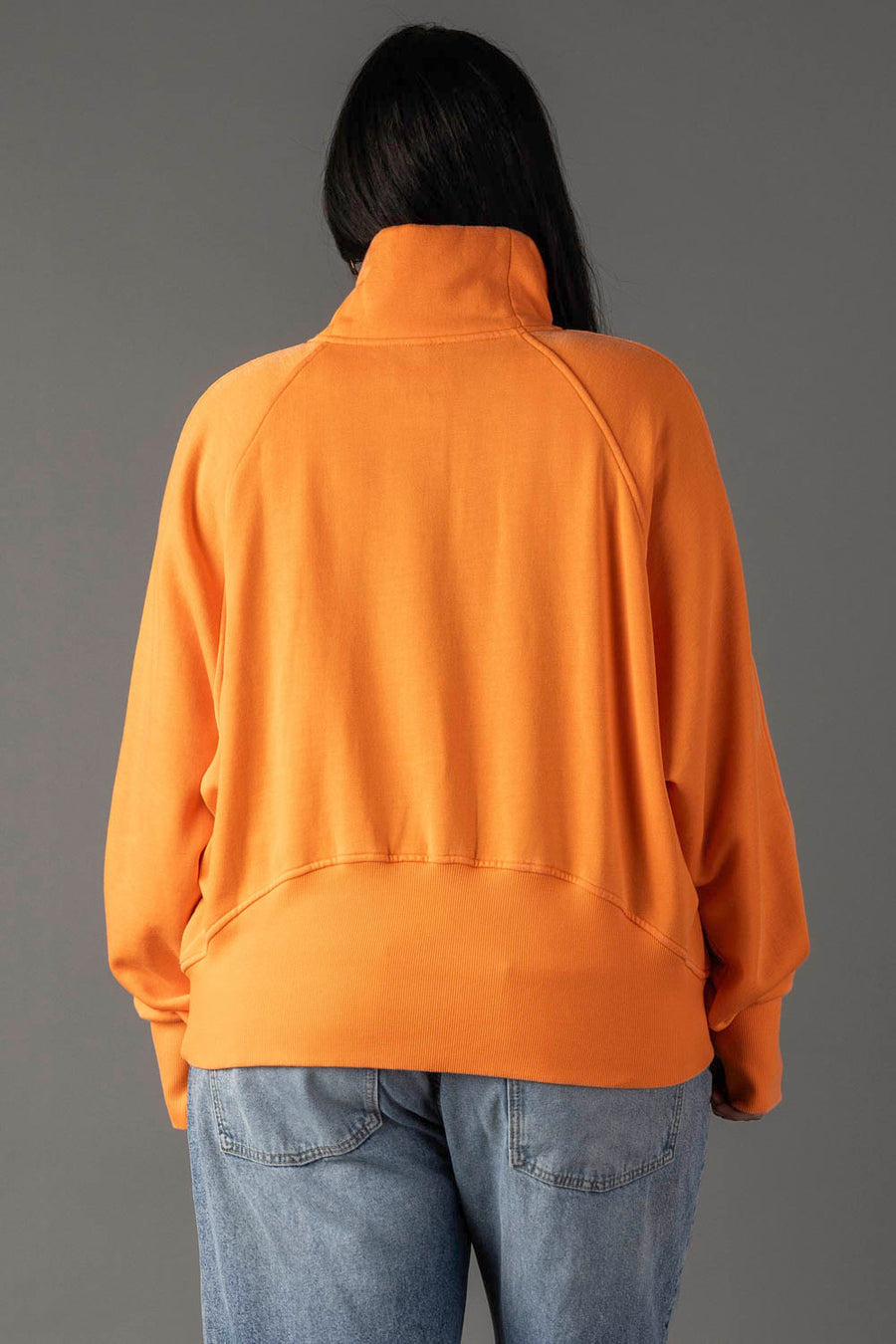 A person with long dark hair is seen from behind, wearing the Panache Apparel Collection Orange Quarter Zip Sweatshirt and light blue jeans, standing against a plain gray background.