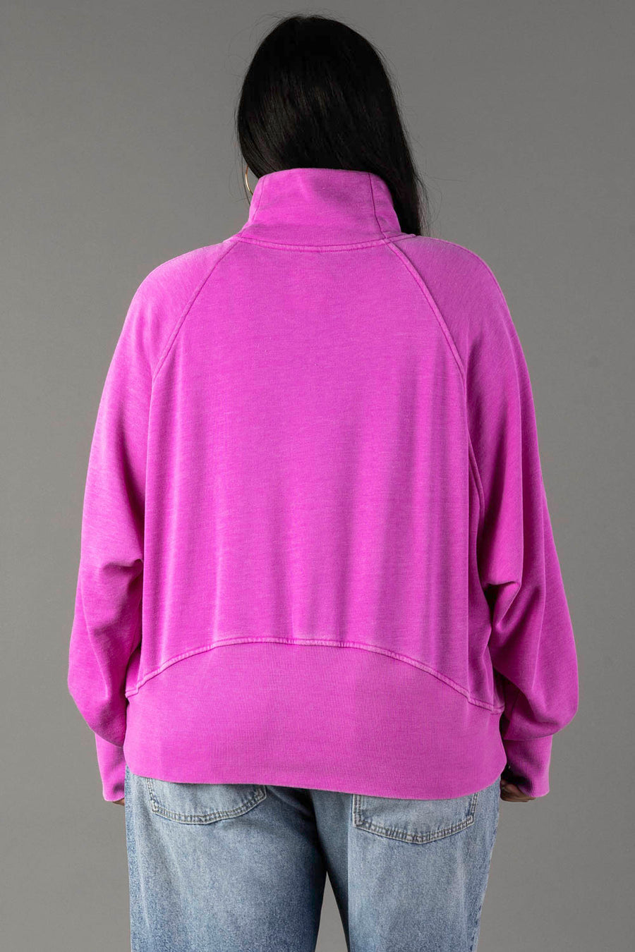 A person with long dark hair is shown from the back, wearing the Panache Apparel Collection’s Purple Quarter Zip Sweatshirt and light blue jeans, standing against a plain gray background.