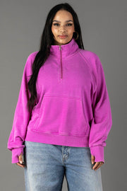 A woman with long dark hair smiles gently at the camera, wearing the Purple Quarter Zip Sweatshirt from Panache Apparel Collection and light blue jeans, standing against a plain gray background.