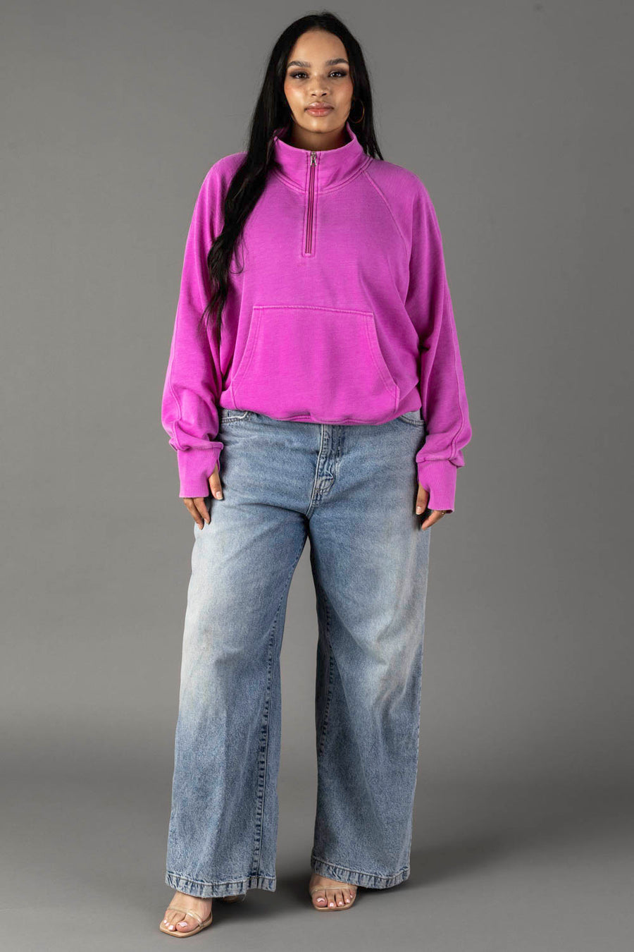 A woman with long, dark hair and a neutral expression wears the Panache Apparel Collection Purple Quarter Zip Sweatshirt against a gray background, paired with light-wash loose jeans and open-toe shoes.