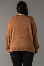 A person with long dark hair is seen from behind, wearing the Panache Apparel Collection’s Brown Whiskey Weather Lightweight Sweater and black pants, standing against a plain gray background.
