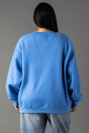 A person with long dark hair, seen from behind, is wearing the Blue Margarita Weather Sweatshirt by Panache Apparel Collection and light blue jeans against a plain gray background.