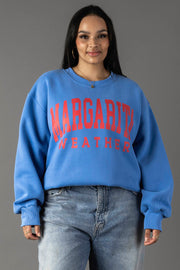A woman with long dark hair wears the Blue Margarita Weather Sweatshirt from Panache Apparel Collection and light blue jeans, standing against a plain gray background.