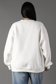 A person with long dark hair is seen from behind against a gray background, wearing the Panache Apparel Collection’s oversized White Coffee Weather Sweatshirt paired with blue jeans.