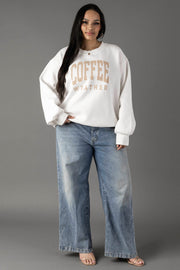 A woman with long dark hair smiles gently at the camera, wearing a Panache Apparel Collection White Coffee Weather Sweatshirt against a gray background, paired with loose blue jeans and beige sandals.