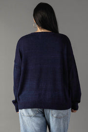 A person with long dark hair wears hoop earrings and the Panache Apparel Collection's Drink On A Boat Lightweight Sweater in navy blue, paired with light blue jeans, standing back to the camera against a plain gray background.