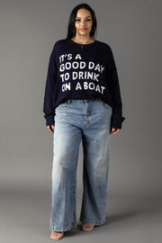 A woman with long dark hair poses against a gray background wearing the Panache Apparel Collection Drink On A Boat Lightweight Sweater in navy and light blue wide-leg jeans, paired with open-toe shoes.