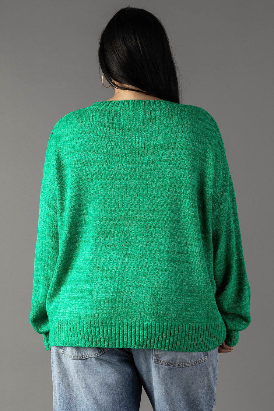 A person with long dark hair wears the Panache Apparel Collection Green Margs Lightweight Sweater and light blue jeans, standing with their back to the camera against a plain gray background.