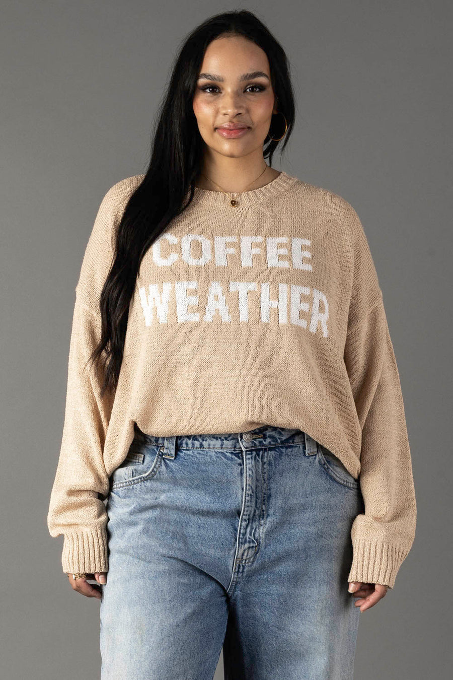 A woman models the Panache Apparel Collection’s Tan & Ivory Coffee Weather Lightweight Sweater against a plain gray background, standing with relaxed hands and a slight smile.
