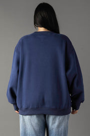 A person with long dark hair, seen from behind, wears the Panache Apparel Collection's Drink At The Cabin Sweatshirt in navy blue with light blue jeans, standing against a plain gray background.