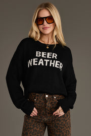 A woman wearing the Panache Apparel Collection’s Beer Weather Lightweight Sweater in black and leopard print pants stands with one hand in her pocket, sunglasses on, against a plain background.