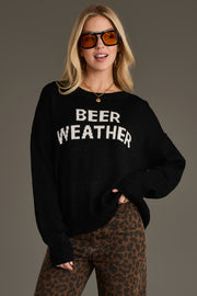 A woman stands against a neutral background, smiling with one hand on her hip. She wears large sunglasses, leopard-print pants, and the Panache Apparel Collection Beer Weather Lightweight Sweater, a cozy knit that adds a playful touch to her bold look.