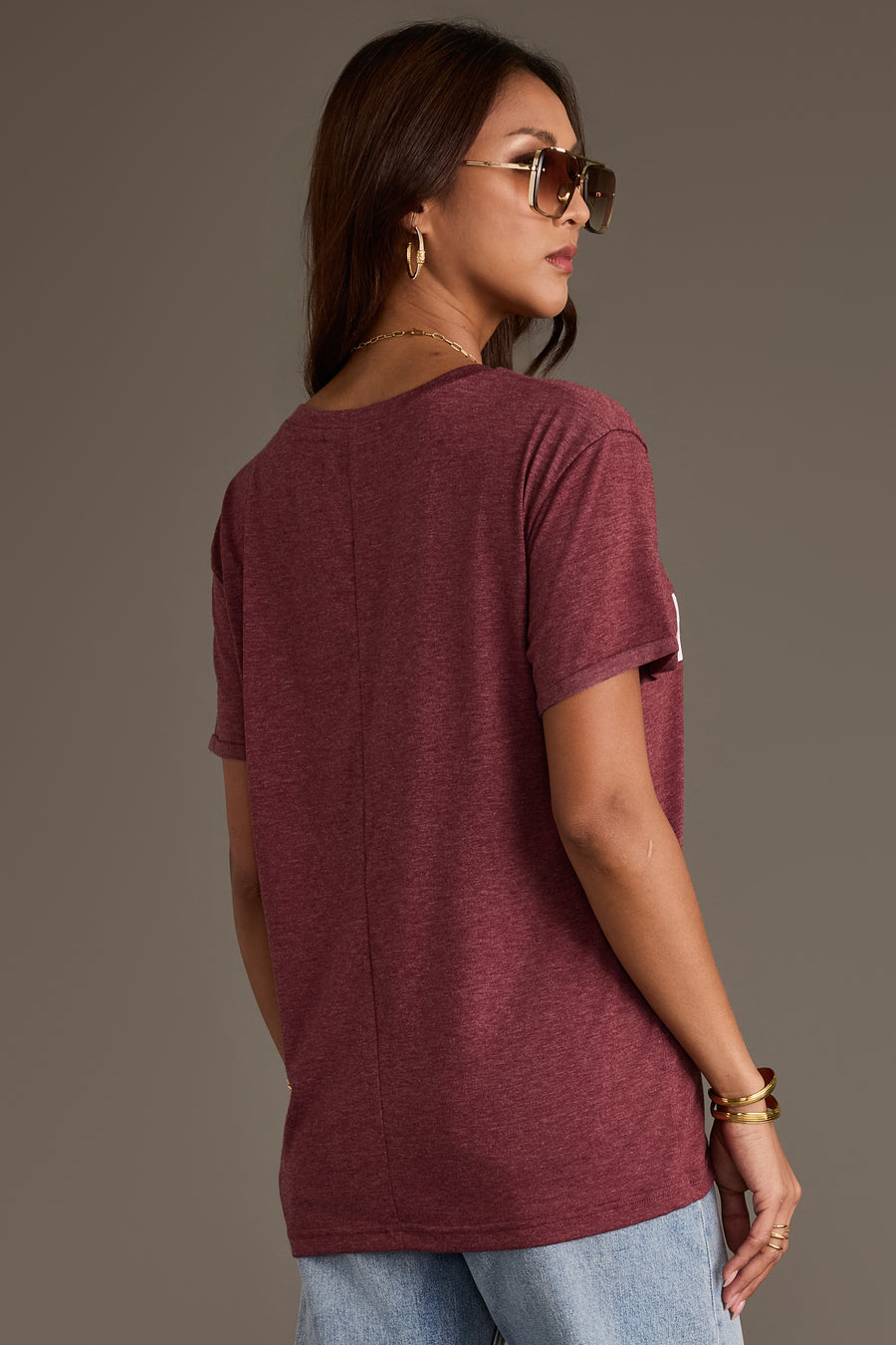 A person seen from behind, wearing a burgundy Wine Weekend Tee and light-wash jeans.