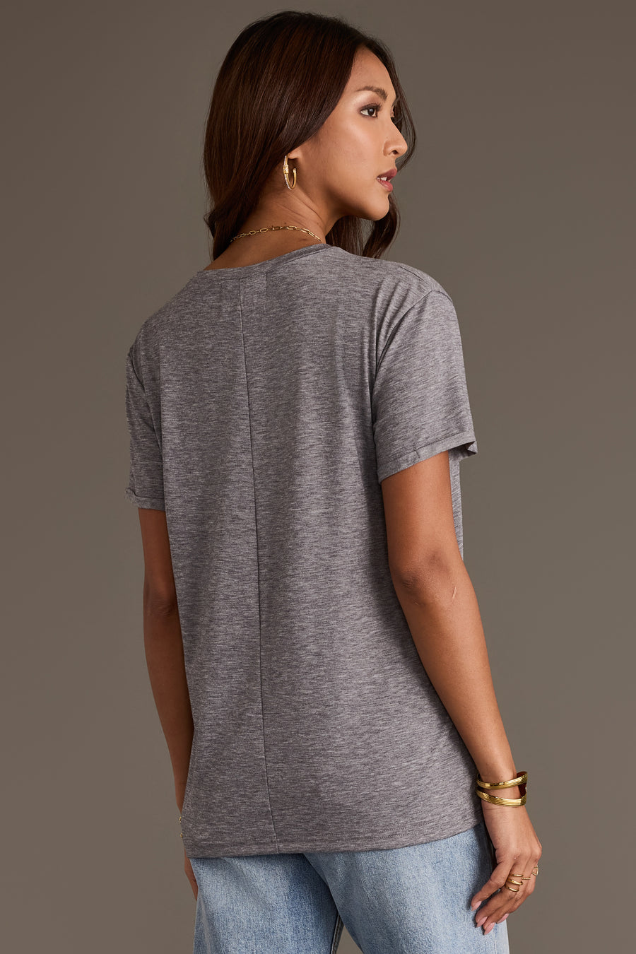A woman seen from behind, wearing a relaxed fit gray Panache Apparel Collection Gray Wine Season Tee with a vertical seam down the center of the back, paired with light-wash jeans.