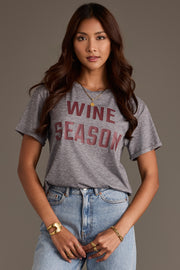 A woman wears a Gray Wine Season Tee with maroon lettering, paired with light-wash blue jeans.