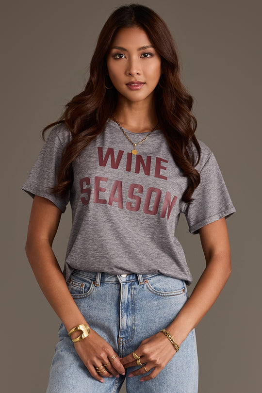 A woman wears a Gray Wine Season Tee with maroon lettering, paired with light-wash blue jeans.