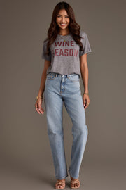 A woman wearing a gray Panache Apparel Collection Gray Wine Season Tee and light-wash blue jeans.