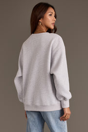 A person seen from the back wearing an oversized gray Panache Apparel Collection Gray Wine Sweatshirt with chenille lettering and blue jeans.