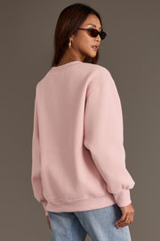 A person wearing an oversized Pink Wine Sweatshirt with chenille lettering and blue jeans.