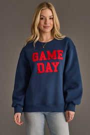 A woman models the Panache Apparel Collection Navy & Red Game Day Sweatshirt, featuring bold red "GAME DAY" lettering, as she smiles against a simple gray backdrop with her hands relaxed at her sides.