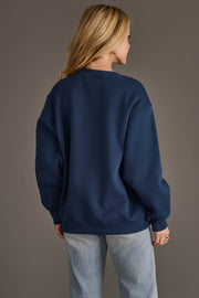 A person with long blonde hair is seen from behind, modeling the Panache Apparel Collection Navy & Red Game Day Sweatshirt paired with light blue jeans, standing against a plain gray background.