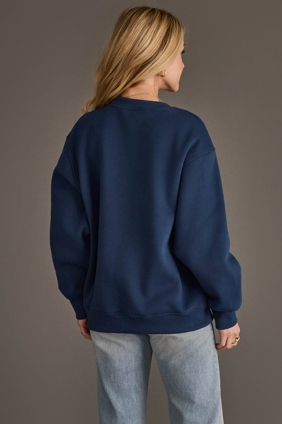 A person with long blonde hair is seen from behind, modeling the Panache Apparel Collection Navy & Red Game Day Sweatshirt paired with light blue jeans, standing against a plain gray background.