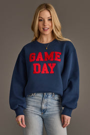 A woman wearing the Panache Apparel Collection's Navy & Red Game Day Sweatshirt, featuring bold red "GAME DAY" lettering, stands against a plain background, smiling at the camera.
