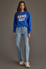 A woman wearing the Royal Blue & White Game Day Sweatshirt by Panache Apparel Collection, paired with light blue jeans and white sneakers, stands against a neutral background, looking at the camera with her arms relaxed at her sides.