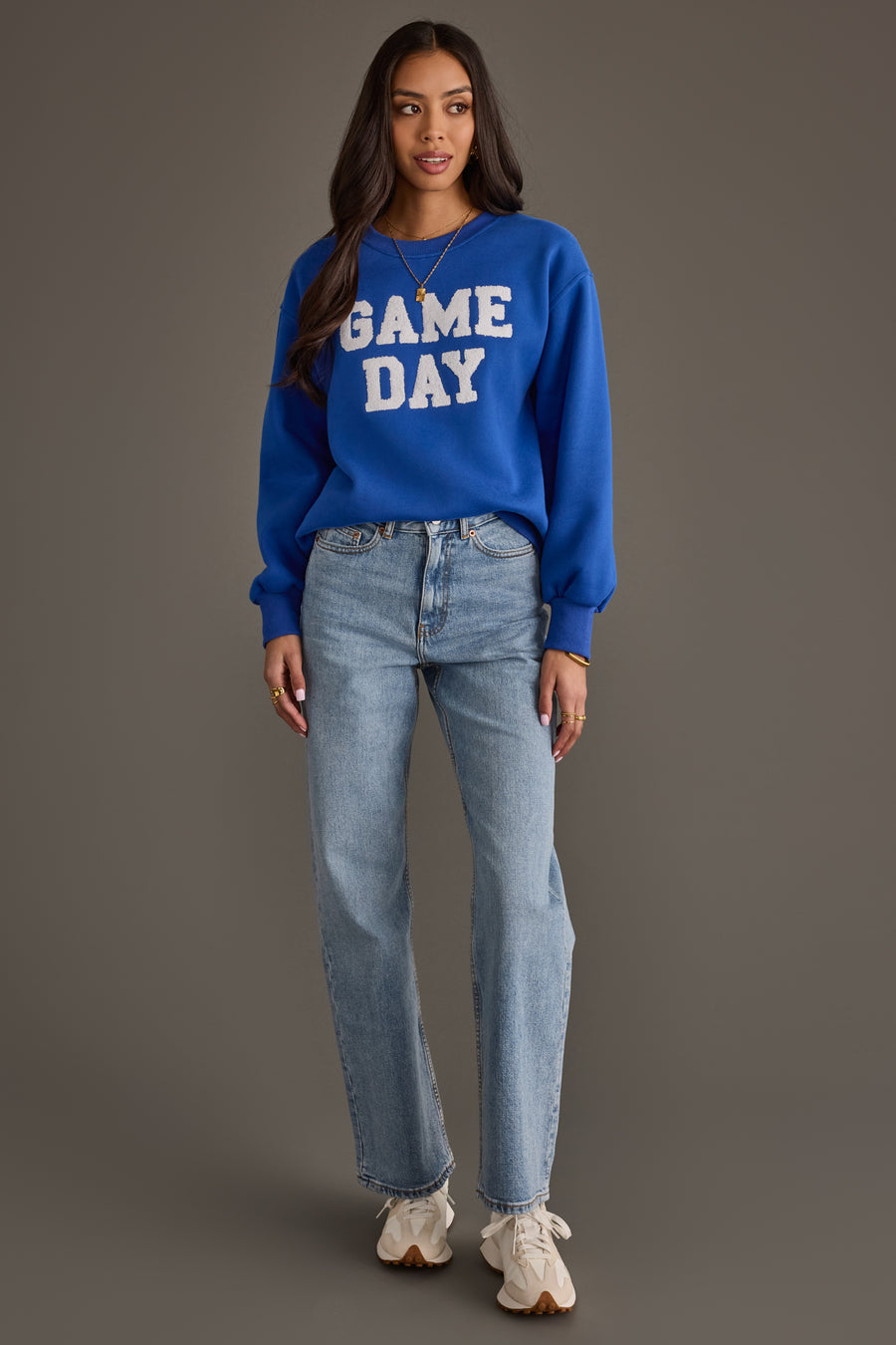 A woman wearing the Royal Blue & White Game Day Sweatshirt by Panache Apparel Collection, paired with light blue jeans and white sneakers, stands against a neutral background, looking at the camera with her arms relaxed at her sides.