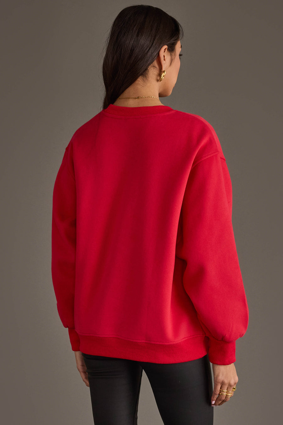 A person with long dark hair, dressed in the Panache Apparel Collection’s Red & Black Game Day Sweatshirt and black pants, stands facing away from the camera against a plain background.