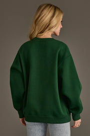 A person with long blonde hair is wearing the Panache Apparel Collection’s Green & Gold Game Day Sweatshirt and light blue jeans, standing against a plain brown background with their back to the camera.