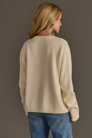 A person with long blonde hair, dressed in the Panache Apparel Collection Cowboy Sweater and blue jeans, stands facing away from the camera against a plain, neutral background.