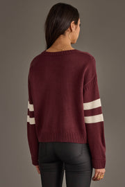 A woman with long dark hair, wearing gold hoop earrings and black pants, stands facing away from the camera against a plain background, showcasing the Panache Apparel Collection Burgundy & White 17 Sweater.