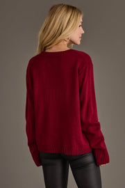 A woman with long blonde hair, dressed in the Panache Apparel Collection’s Maroon & Gold Game Day Sweater and black leather pants, is standing and facing away from the camera against a plain background.