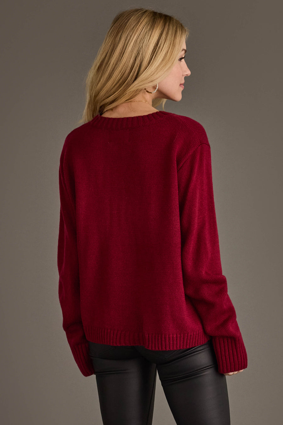 A woman with long blonde hair, dressed in the Panache Apparel Collection’s Maroon & Gold Game Day Sweater and black leather pants, is standing and facing away from the camera against a plain background.