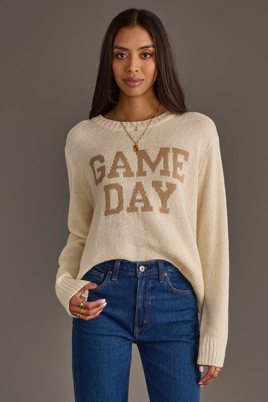 A woman with long dark hair wears the Panache Apparel Collection's Ivory Game Day Lightweight Sweater and blue jeans, standing against a plain gray background.