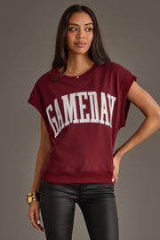 A woman wearing the Panache Apparel Collection Maroon & White Game Day Short Sleeve Sweatshirt with bold white lettering, paired with black leather pants and gold jewelry, stands against a plain gray background.
