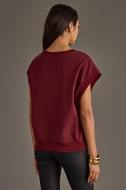 A woman with long dark hair, wearing the Panache Apparel Collection’s Maroon & White Game Day Short Sleeve Sweatshirt, black pants, gold hoop earrings, and bracelets, stands facing away from the camera against a neutral background.