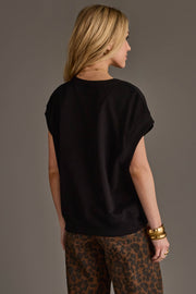 A woman with long blonde hair stands facing away against a plain gray background, wearing the Panache Apparel Collection’s Black & Light Brown Game Day Short Sleeve Sweatshirt and several gold bracelets.