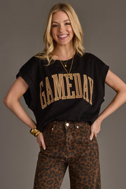 A smiling woman with long blonde hair wears the Panache Apparel Collection’s Black & Light Brown Game Day Short Sleeve Sweatshirt paired with high-waisted leopard print pants and gold jewelry, standing against a plain background.