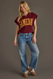 A woman stands against a gray background wearing the Panache Apparel Collection’s Maroon & Gold Game Day Short Sleeve Sweatshirt, paired with blue jeans and brown sneakers. She has long blonde hair and strikes a relaxed pose, with one hand in her pocket.