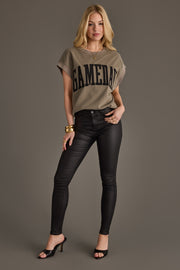 A woman stands confidently wearing a Panache Apparel Collection Gray/Olive & Black Game Day Short Sleeve Sweatshirt, black leather-look skinny jeans, black heels, and gold jewelry, posing against a plain gray background.