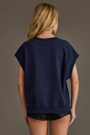 A woman with long blonde hair is standing with her back to the camera, wearing the Panache Apparel Collection Navy & White Game Day Short Sleeve Sweatshirt and black shorts against a plain gray background.