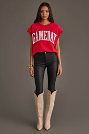 A woman stands against a plain gray background wearing the Panache Apparel Collection Red & White Game Day Short Sleeve Sweatshirt, black skinny jeans, tan cowboy boots, and gold bracelets.
