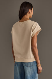 A woman with long dark hair wears the Panache Apparel Collection Beige & Gray Game Day Short Sleeve Sweatshirt, along with blue jeans, gold hoop earrings, and bracelets. She stands facing away from the camera against a plain brown background.