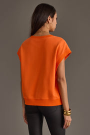 A woman stands facing away against a plain gray background, wearing the Panache Apparel Collection Orange & White Game Day Short Sleeve Sweatshirt, paired with black pants, gold hoop earrings, and gold bracelets.
