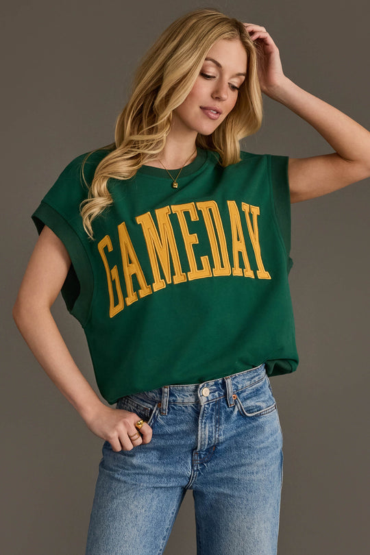 A woman stands against a plain background, posing with one hand on her hip and the other touching her hair, wearing the Panache Apparel Collection's Green & Gold Game Day Short Sleeve Sweatshirt paired with blue jeans.