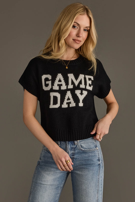 A person with long blonde hair wears the Black & White Game Day Short Sleeve Sweater by Panache Apparel Collection, paired with light blue jeans and standing against a plain background.
