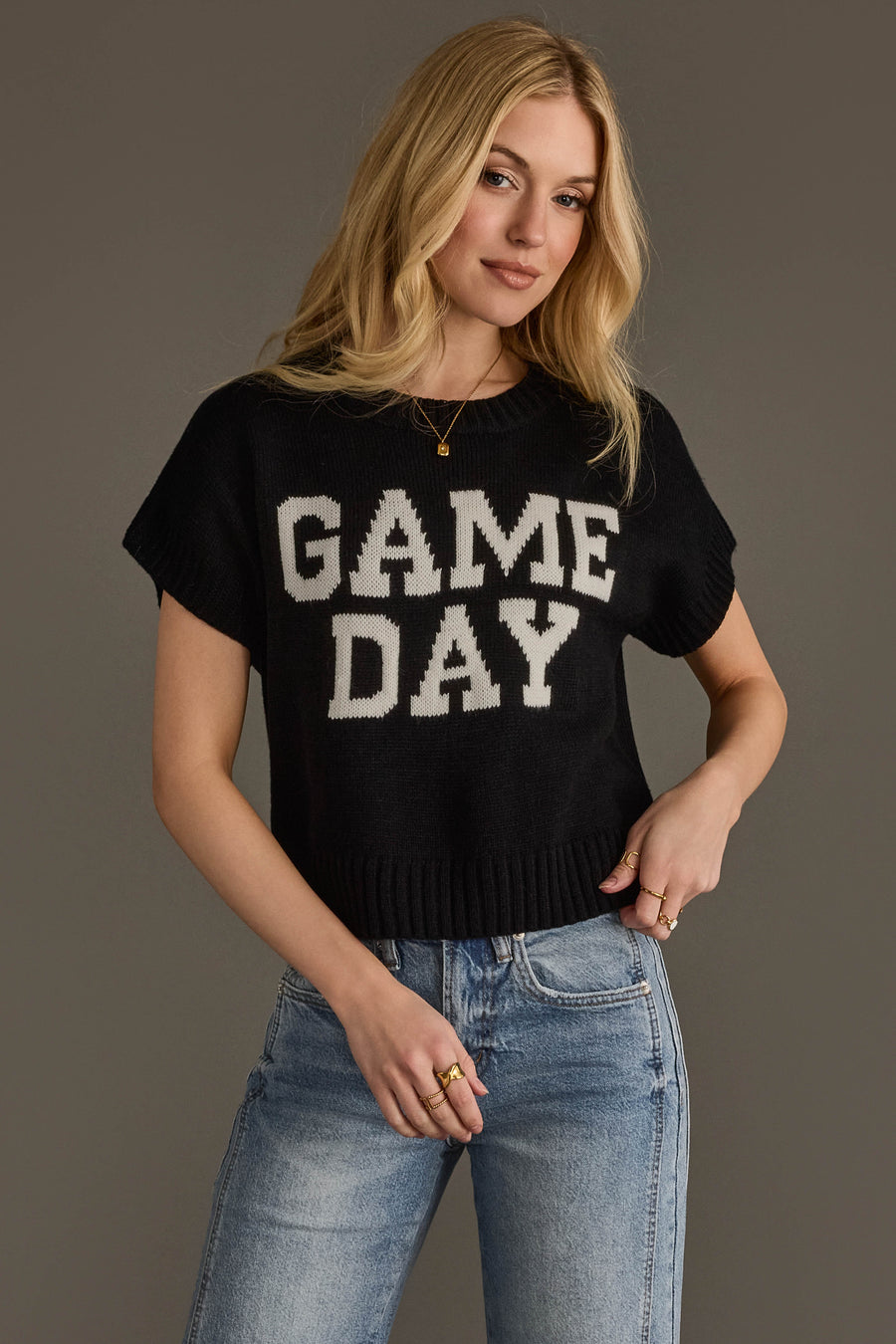 A person with long blonde hair wears the Black & White Game Day Short Sleeve Sweater by Panache Apparel Collection, paired with light blue jeans and standing against a plain background.