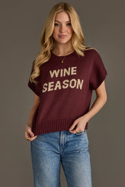 A person is seen wearing the Panache Apparel Collection's Wine Season Short Sleeve Sweater—maroon with "WINE SEASON" printed in white—paired with blue jeans, standing against a plain gray background.